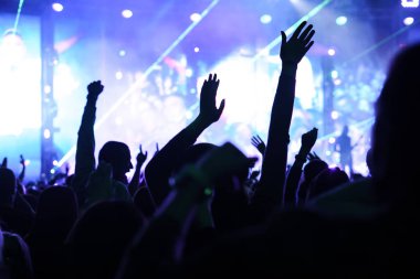 Seyirci bir Müzik Festivali ve sahne yukarıdan aşağı akış ışıklar kaldırdı elleriyle. Yumuşak odak, yüksek ISO, grenli görüntü.