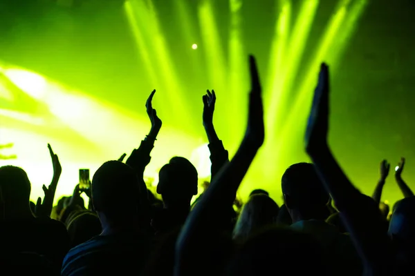 Publikum mit erhobenen Händen bei einem Musikfestival und Lichtern, die von der Bühne herabströmen. Weicher Fokus, hohe Isozahl, körniges Bild. — Stockfoto