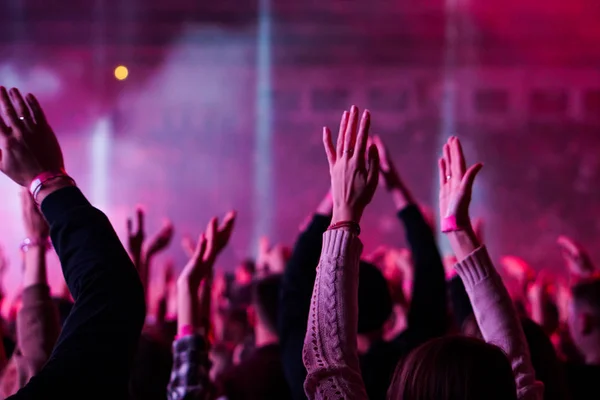 Publik med händerna upp på en musikfestival och ljus strömmande ner från scenen. Mjukt fokus, höga Iso, kornig bild. — Stockfoto