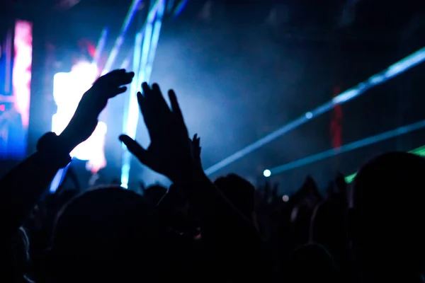 Pubblico con le mani alzate a un festival musicale e luci che scendono dal palco. Focus morbido, alta ISO, immagine granulosa . — Foto Stock