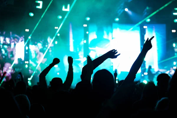 Pubblico con le mani alzate a un festival musicale e luci che scendono dal palco. Focus morbido, alta ISO, immagine granulosa . — Foto Stock