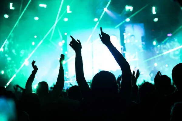 Público con las manos levantadas en un festival de música y luces que fluyen desde arriba del escenario. Enfoque suave, alta ISO, imagen granulada . — Foto de Stock