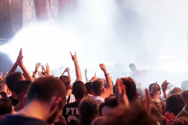 Audience with hands raised at a music festival and lights streaming down from above the stage. Soft focus, high ISO, grainy image. — Stock Photo, Image