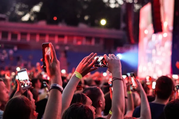 Audience with hands raised at a music festival and lights streaming down from above the stage. Soft focus, high ISO, grainy image. — Stock Photo, Image