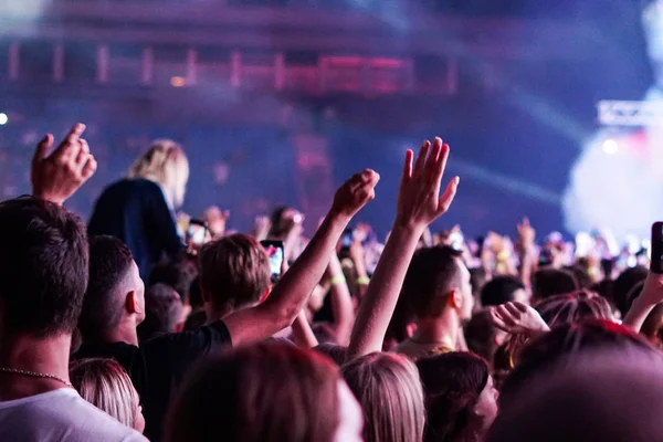 Publikum mit erhobenen Händen bei einem Musikfestival und Lichtern, die von der Bühne herabströmen. Weicher Fokus, hohe Isozahl, körniges Bild. — Stockfoto