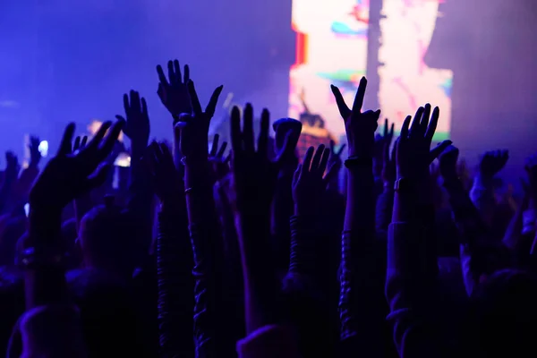 Pubblico con le mani alzate a un festival musicale e luci che scendono dal palco. Focus morbido, alta ISO, immagine granulosa . — Foto Stock