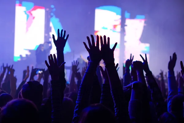 Audience with hands raised at a music festival and lights streaming down from above the stage. Soft focus, high ISO, grainy image. — Stock Photo, Image