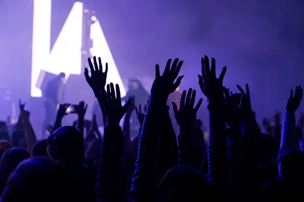 Auditoire avec les mains levées lors d'un festival de musique et des lumières descendant d'en haut de la scène. Mise au point douce, ISO élevé, image granuleuse . — Photo