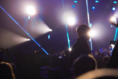 Çocuk bir açık hava rock müzik konserinde onlarla el ele tutuşarak ailesinin omuzlarında eğlenceli