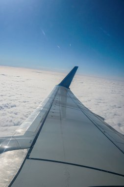 Bulutların üzerinde uçan bir uçağın kanadı. İnsanlar uçağın penceresinden gökyüzüne bakıyorlar, seyahat etmek için hava ulaşımını kullanıyorlar..