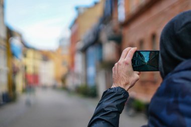 Şık, akıllı telefonlu çekici bir gezgin arka plandaki palmiye ağacında eski bir binanın fotoğrafını çekiyor. Boş kare ve mavi gökyüzü.