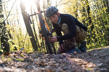Yorgun bir adam ormanda oturur, dinlenir ve bir bisiklete bakar.