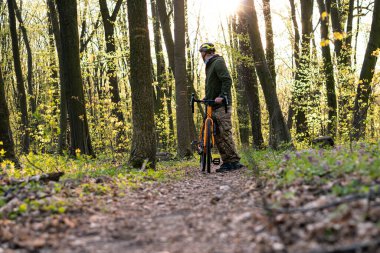 Bisikletçi elinde bisikletle orman yolunda yürüyor.