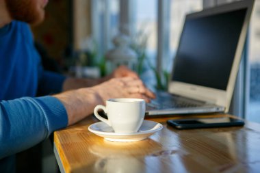 Bir adam bir laptop bir fincan kahve yanında oturuyor