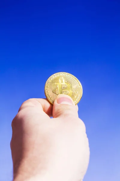 Kripto para birimi. Bitcoin. Bir el kaldırdı mavi gökyüzüne karşı bir altın sikke bit sikke tutar. Güneş ışınları madeni para yansıtılır.