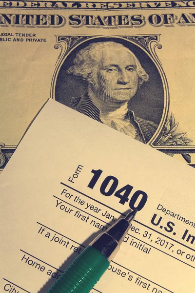 Tax day. The tax form 1040, green pen and dollar is on a wooden table.