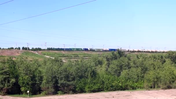 Dlouhý nákladní vlak se stavebními materiály se v létě pohybuje po železnici na pozadí polí a lesů za slunečného dne. — Stock video