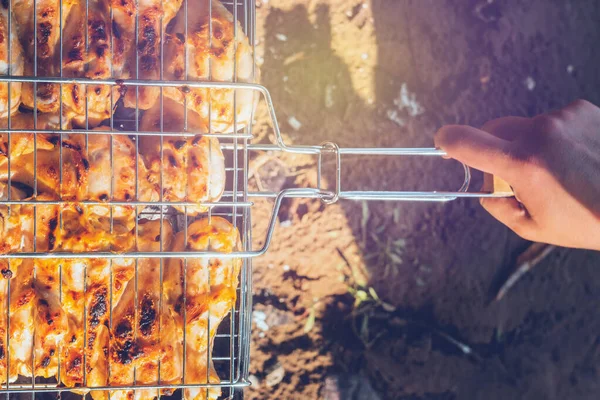 Vařím grilované kuře na uhlících na grilu. Selektivní soustředění. Matice s kuřetem nad žhavým uhlím. Rozmazané pozadí. Kuřecí křidýlka se pokládají na gril. Detailní záběr. — Stock fotografie