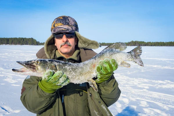 Man of Caucasian appearance with a beard holds a large fish pike trophy. Winter fishing winter sport — Stock Photo, Image