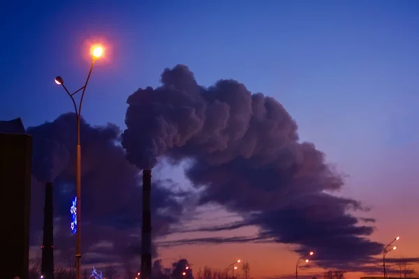 Rauchentwicklung in der Pfeifenfabrik am Abend im Hintergrund der Stadt — Stockfoto