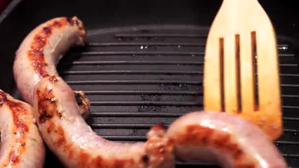Delicious grilled pork sausages rollin on hot grill pan from overhead. — Stock Video