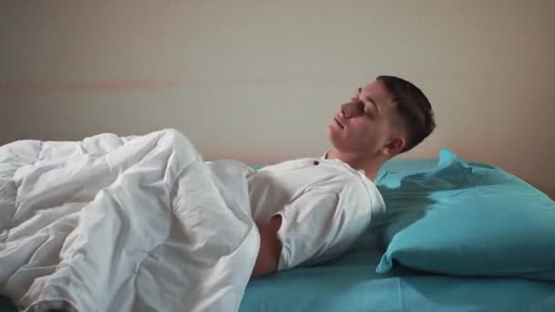 Young man goes to bed, falls asleep in a comfortable bed. Sleeping man — Stock Video