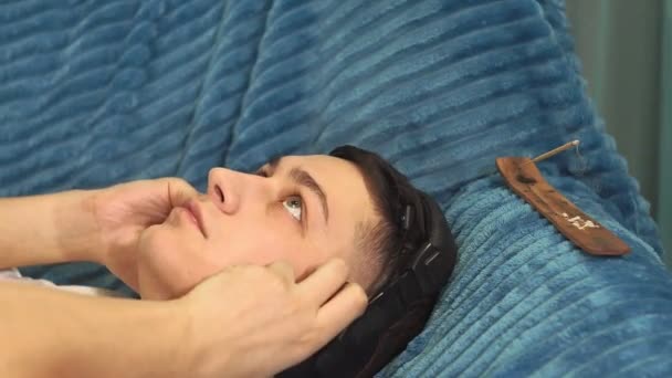 Joven está descansando en el sofá con auriculares primer plano en casa escuchando música relajante, música tranquila. relajación, tranquilidad. auriculares y escuchar música — Vídeo de stock