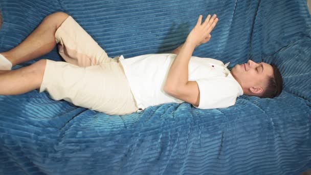 Un giovane uomo è sdraiato sul divano in un telefono cellulare — Video Stock
