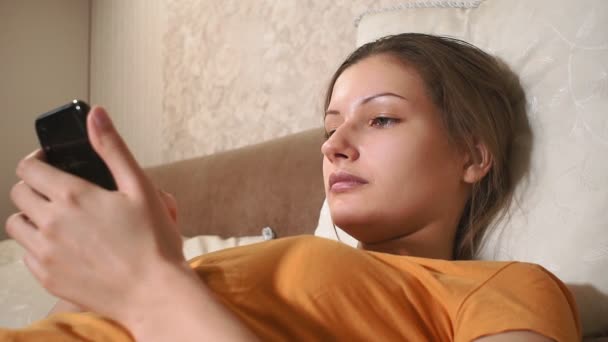 Cara de mujer joven. Retrato de mujer feliz divertirse en la cama. utiliza un teléfono móvil — Vídeos de Stock