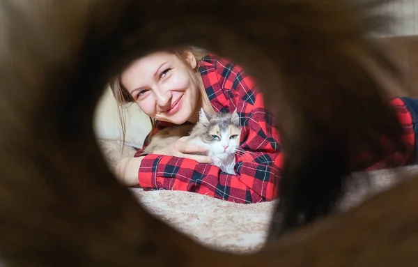 Young girl portrait close-up lying on the sofa with a cat looking at the camera. house favourite. shot through the tail of a passing dog — Stock Photo, Image