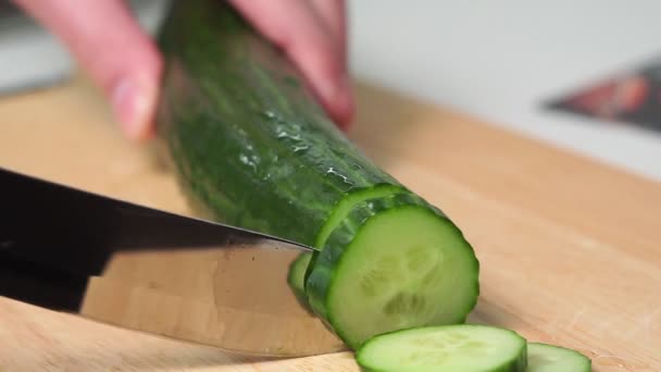 Skär av gurkan. En man med händerna skär en gurka med kniv på en träskiva. ingrediens för sallad — Stockvideo