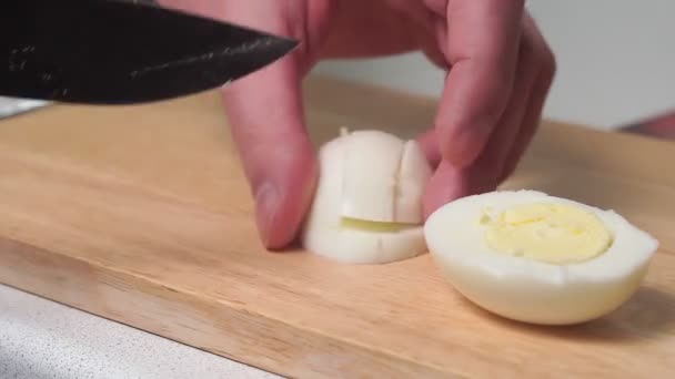Homem corta um ovos cozidos em círculos com uma faca grande em uma placa de cozinha na cozinha em casa. ingrediente de salada de cozinha caseira — Vídeo de Stock