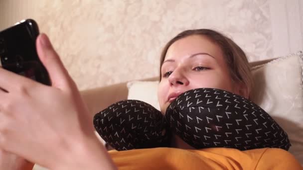 Young girl is lying on the sofa looking at her mobile phone, browsing social networks. laughing, smiling — Stok video