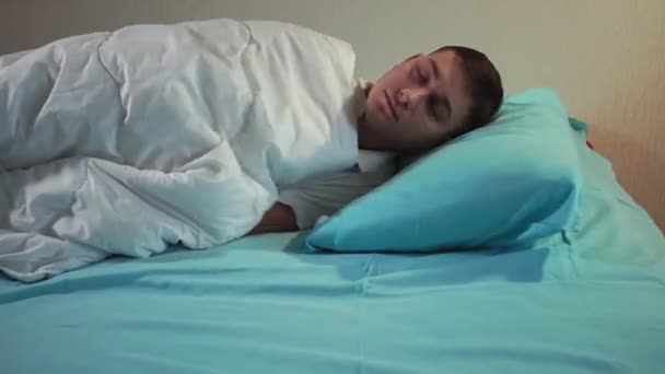 Молодой человек ложится спать с включенным светом в уютной кровати. Спокойный сон — стоковое видео