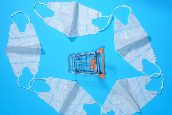 Concept of purchasing personal protective equipment against respiratory organs and viruses. Medical mask in a shopping cart on a blue background. Flat lay — 스톡 사진