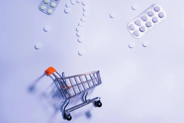 Small shopping trolley on blue background. Drugs, medicine, food supplements, choice of buying pills. — Stok fotoğraf