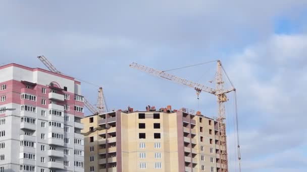 Bouwkranen en arbeiders bouwen huizen met meerdere verdiepingen — Stockvideo