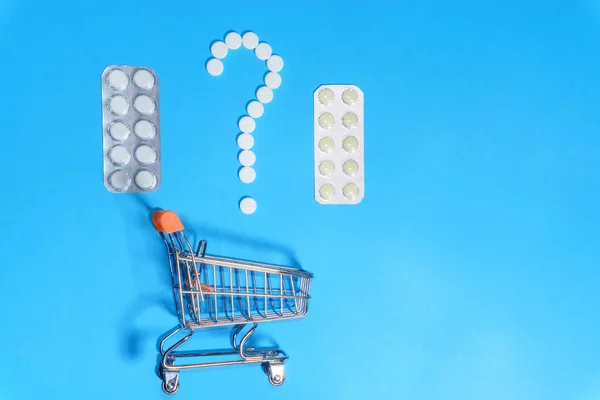 shopping cart of pills. Blue background. Concept: Health using medicines. purchase tablets, variety of tablets, question mark