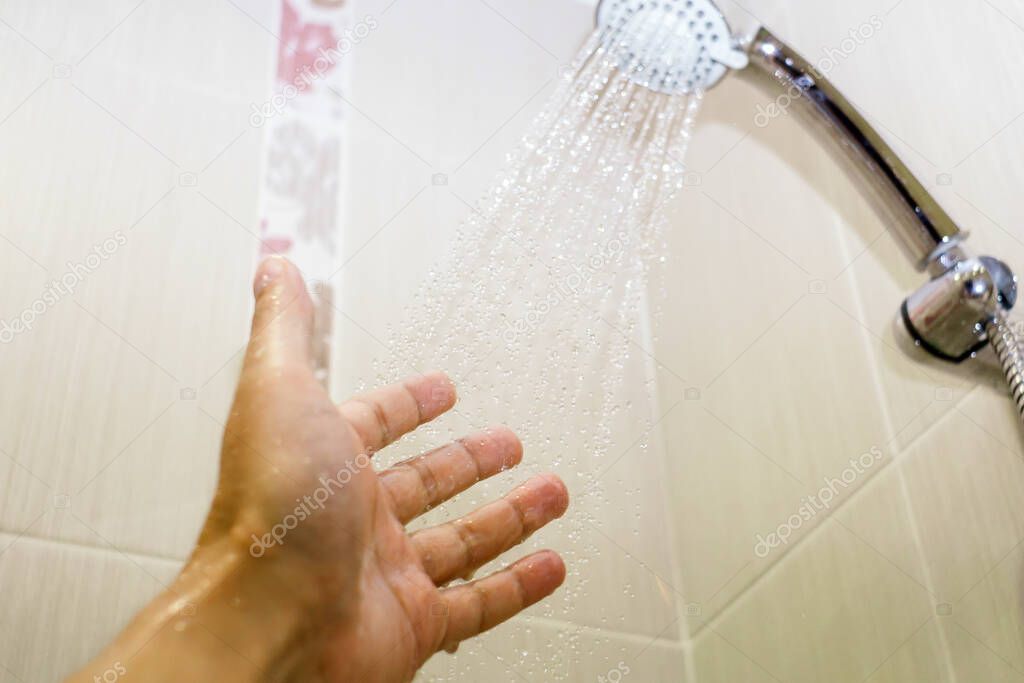 Close-up of a man hand check water temperature in the shower with hand shower wall. selective focus