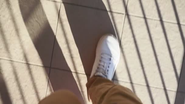 Beyaz spor ayakkabılı bir adam güneşli bir günde sokakta yürür. pov video, birinci şahıs — Stok video
