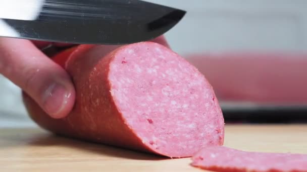 Corte salsicha defumada com faca. As fatias de linguiça estão em um close-up de tábua de corte. Cozinhe as fatias de carne — Vídeo de Stock
