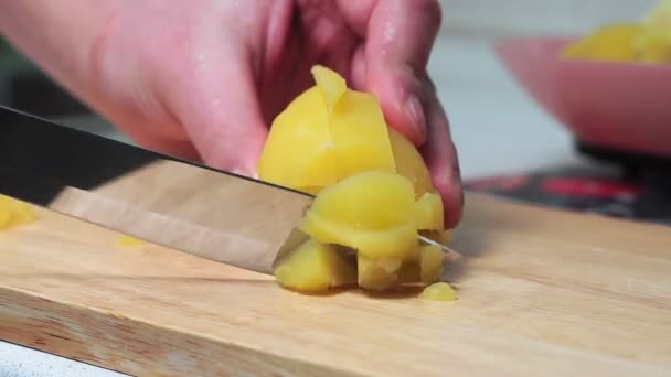 Gekookte aardappelen snijden. maak handen snijden gekookte aardappelen met een groot mes op een houten snijplank. thuis koken, salade ingrediënt — Stockvideo