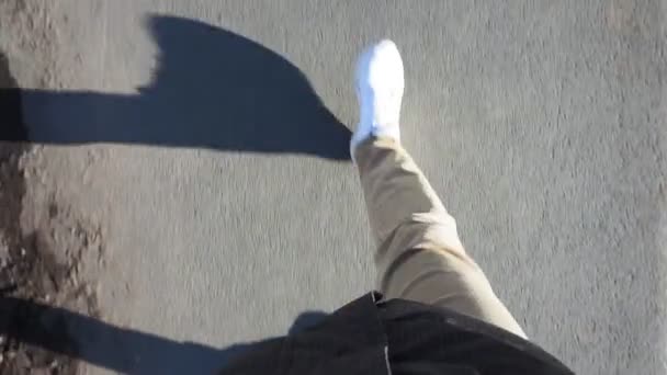 Homem de tênis branco caminha no pavimento em jeans em um dia ensolarado brilhante. pov vídeo, primeira pessoa — Vídeo de Stock