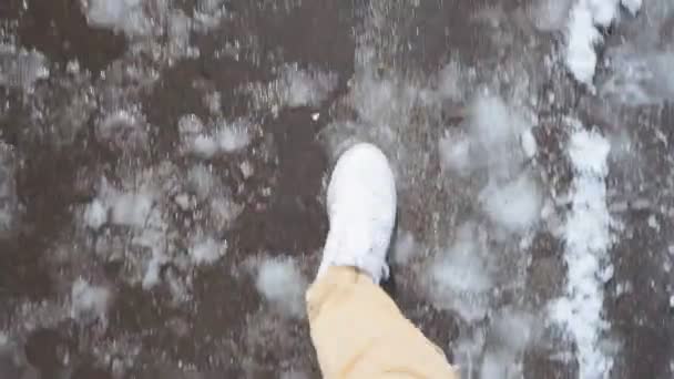 Белые кроссовки прогуливаются по мокрому асфальтовому тротуару в снежном POV видео — стоковое видео