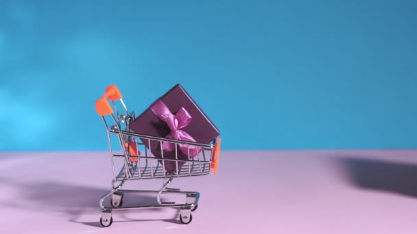 Nákupní košík s dárkem, prostor pro text na modrém pozadí, kopírovací prostor. koncept nakupování, dárek na dovolenou, narozeniny — Stock video