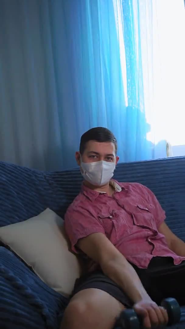 Молодий чоловік займається спортом вдома гантелі в масці гумор вертикальне відео — стокове відео
