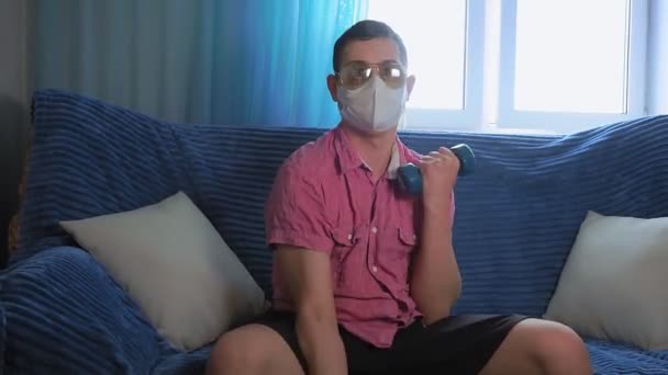 Evde spor yapan genç bir adam, maskeli bir dambıl. Evde kal. mizah — Stok video