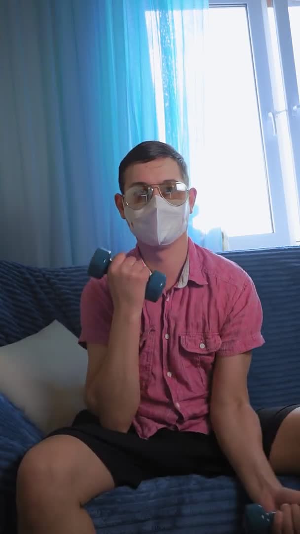 Молодий чоловік займається спортом вдома, гантелі в масці від коронавірусу — стокове відео
