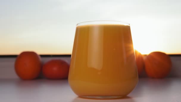 Vidro de suco de laranja e frutas de laranjas, foco seletivo. ao pôr do sol, lugar para texto, espaço de cópia — Vídeo de Stock