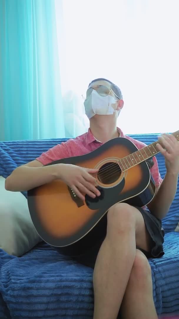 Toca la guitarra con una máscara de un coronavirus. Vídeo vertical, humor — Vídeos de Stock